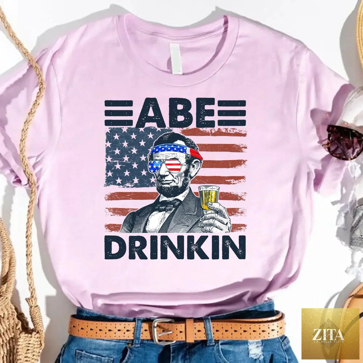A black Abraham Lincoln patriotic T-shirt with "Abe Drinkin" and 4th of July design, featuring Lincoln's portrait and American flags.