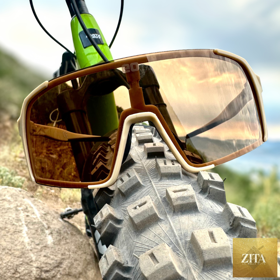 Eastern Outer Uno Mas Photochromic+ sunglasses with khaki brown frames and tinted lenses, outdoor scene with tire background.