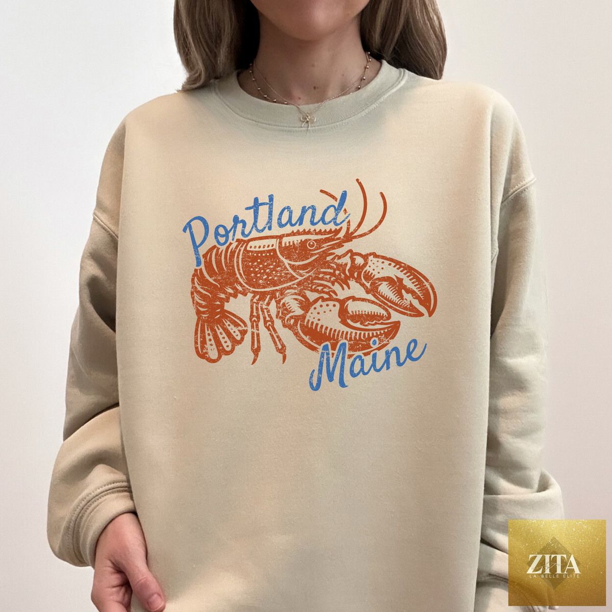 Portland Maine Lobster Crewneck Sweatshirt by Zita La Belle Elite featuring a coastal lobster graphic on beige fabric.
