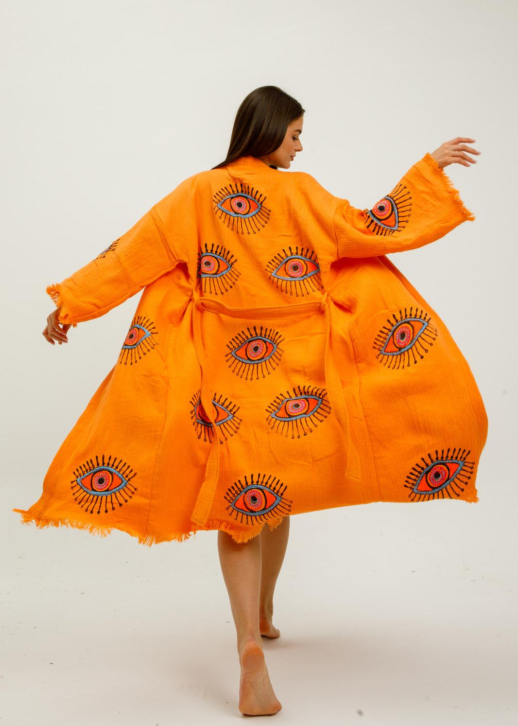 Hand-printed orange evil eye kimono by Buldano featuring natural fabric and intricate design, displayed on a hanger.